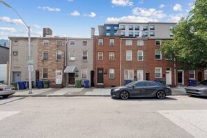 A row of townhouses with a street in front, trash bins, and a parked car. - Stylish 3-bedroom, 3-bath townhome in one of Baltimore's most walkable neighborhoods steps from Little Italy, Fells Point's cobblestone streets, and the Inner Harbor waterfront (Baltimore)