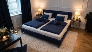 A bedroom with a large bed, two bedside tables, a nightstand, a window with curtains, and a small table with a vase and glasses. - The Gem of Downtown: Scenic Boutique Hideaway by the Promenade – 312 (Budapest)