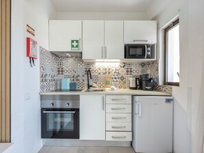 Eine kompakte Küche mit weißen Schränken, einer Mikrowelle, einer Kaffeemaschine und einem kleinen Kühlschrank.