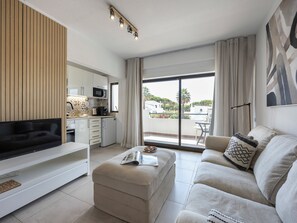 Ein modernes Wohnzimmer mit Flachbildfernseher, einem beigefarbenen Sofa, einem Couchtisch und einer Küchenzeile mit Mikrowelle.