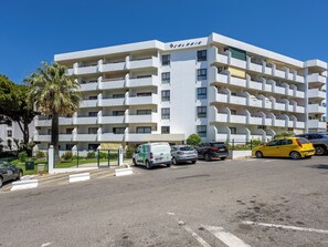 Un edificio de varios pisos con balcones, un área de estacionamiento y un cielo azul despejado.