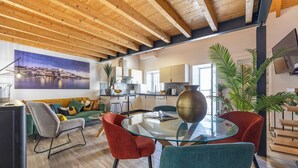 A modern living room with a glass coffee table, red and teal chairs, a wooden ceiling, and a kitchen in the background. - Casa Abraço - River View Terrace in Ferragudo (Ferragudo)