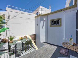 A small outdoor dining area with a table and chairs, a potted plant, and a bottle of wine on a wooden table. - Casa Abraço - River View Terrace in Ferragudo (Ferragudo)