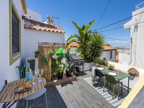 Eine Dachterrasse mit Essbereich, einem Grill und verschiedenen Kübelpflanzen.