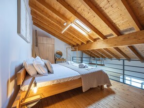 Ein Schlafzimmer mit Holzboden, einem Bett mit Kissen, einer Nachttischlampe und Blick durch ein Fenster.