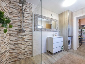 Une salle de bain moderne avec un mur en pierre, une douche en verre, un meuble-lavabo blanc et un meuble en bois.