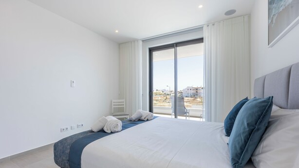 A modern hotel room with a large bed, a view through a sliding glass door, and a chair by the window. - Lagos Odyssey - Sea Views and Dona Ana Bay (Lagos)