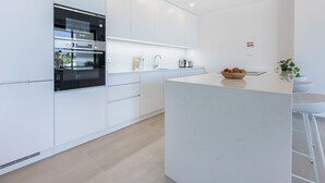 A modern kitchen with white cabinetry, a built-in oven, and a central island with a bowl of fruit. - Lagos Odyssey - Sea Views and Dona Ana Bay (Lagos)