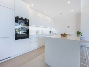 A modern kitchen with white cabinetry, a built-in oven, and a central island with a bowl of fruit. - Lagos Odyssey - Sea Views and Dona Ana Bay (Lagos)