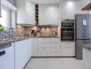 A modern kitchen with white cabinetry, a built-in oven, a stainless steel refrigerator, and a coffee maker on the countertop. - Casa Benção - Sea View and Pool in Lagos (Lagos)