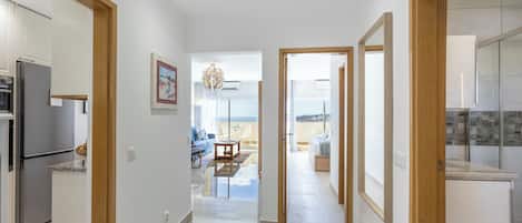 A modern kitchen with a refrigerator, a dining area with a table and chairs, and a hallway leading to a balcony with a view.