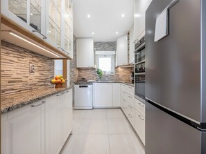 Eine moderne Küche mit weißen Schränken, einem Edelstahlkühlschrank und einer Arbeitsplatte aus Granit.