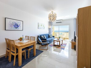 A modern living room with a dining area, a sofa, and a view of the sea through a sliding glass door. - Casa Benção - Sea View and Pool in Lagos (Lagos)