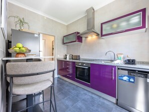 A modern kitchen with purple cabinets, stainless steel appliances, and a bar stool. - Casa Horizonte - Old Town Lagos (Lagos)