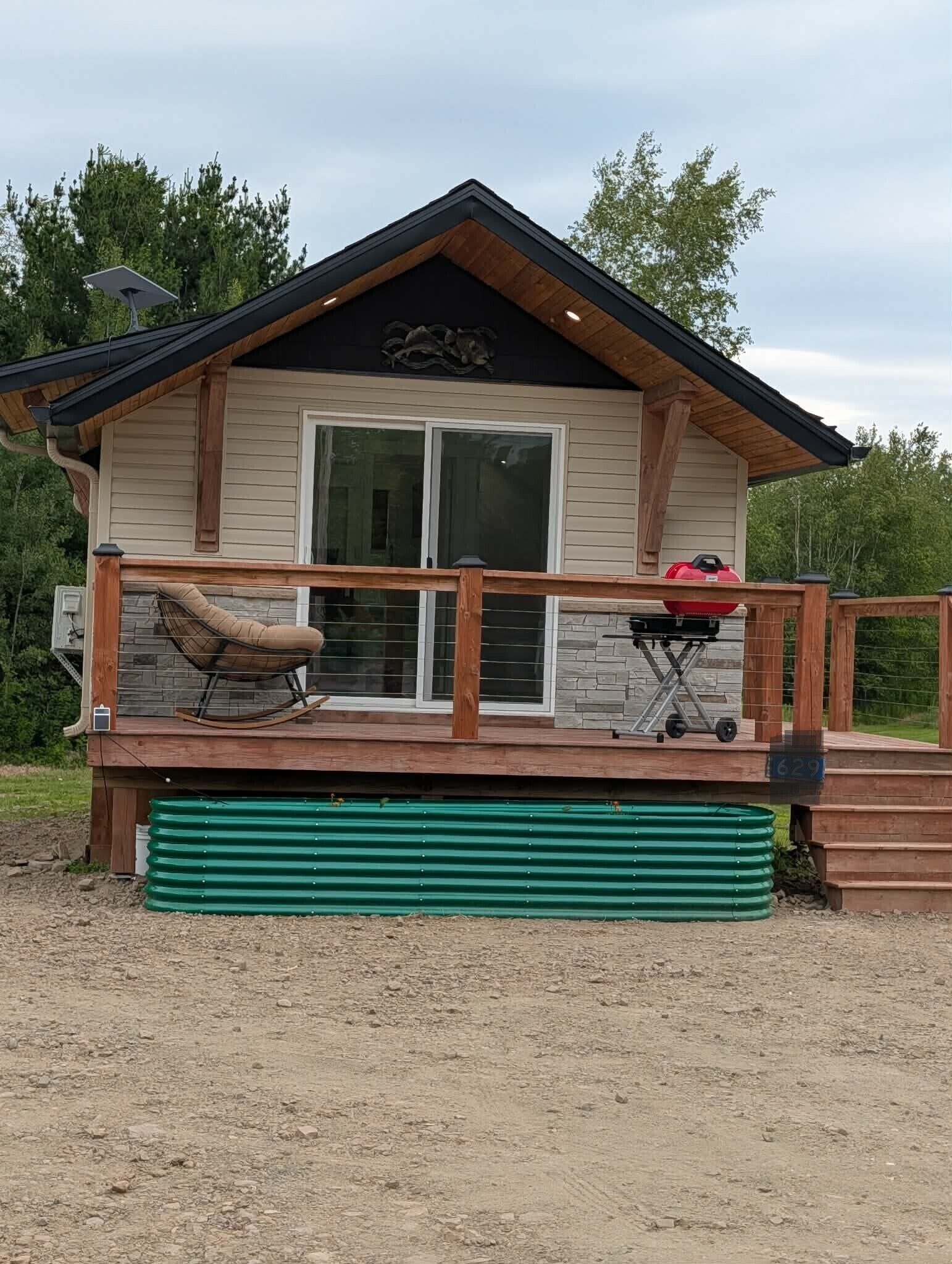 A cabin with a deck, a grill, and a swing chair.