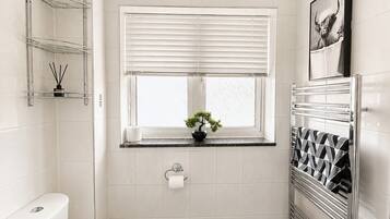 A modern bathroom with a toilet, a window with blinds, a radiator, and a shelf with a plant.