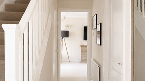 A hallway with a carpeted staircase, white walls, and a door leading to another room.