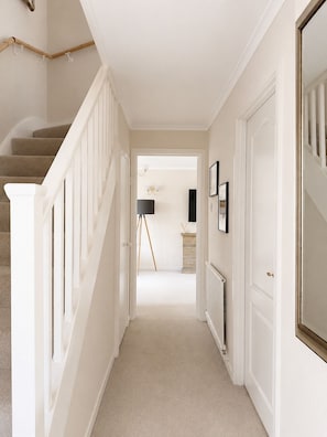A hallway with a carpeted staircase, white walls, and a door leading to another room.
