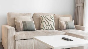 A beige upholstered sectional sofa with a white coffee table and a remote control on it. - StayShort - Stylish 1 Bedroom in JVC - Sleeps 4 (JVC)