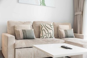 Ein beigefarbenes, bezogenes Ecksofa mit einem weißen Couchtisch und einer Fernbedienung darauf.