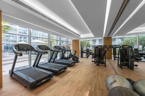 Una palestra moderna con tapis roulant, macchinari ellittici e attrezzature per pesi. Ampie finestre offrono luce naturale e vista all'esterno.