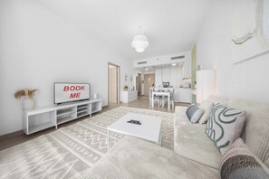 A modern living room with a flat-screen TV, a sofa, a coffee table, and a dining area in the background. - StayShort - Stylish 1 Bedroom in JVC - Sleeps 4 (JVC)