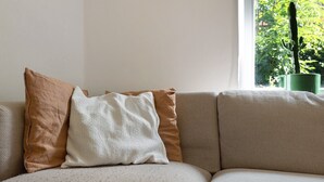 En soffa med tre kuddar och en grön växt i ett fönster.