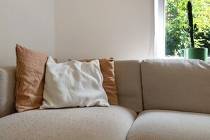 Um sofá com três almofadas e uma planta verde numa janela.