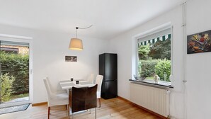 Ett modernt kök med ett svart kylskåp, ett matbord med stolar och ett fönster med utsikt över grönområden.