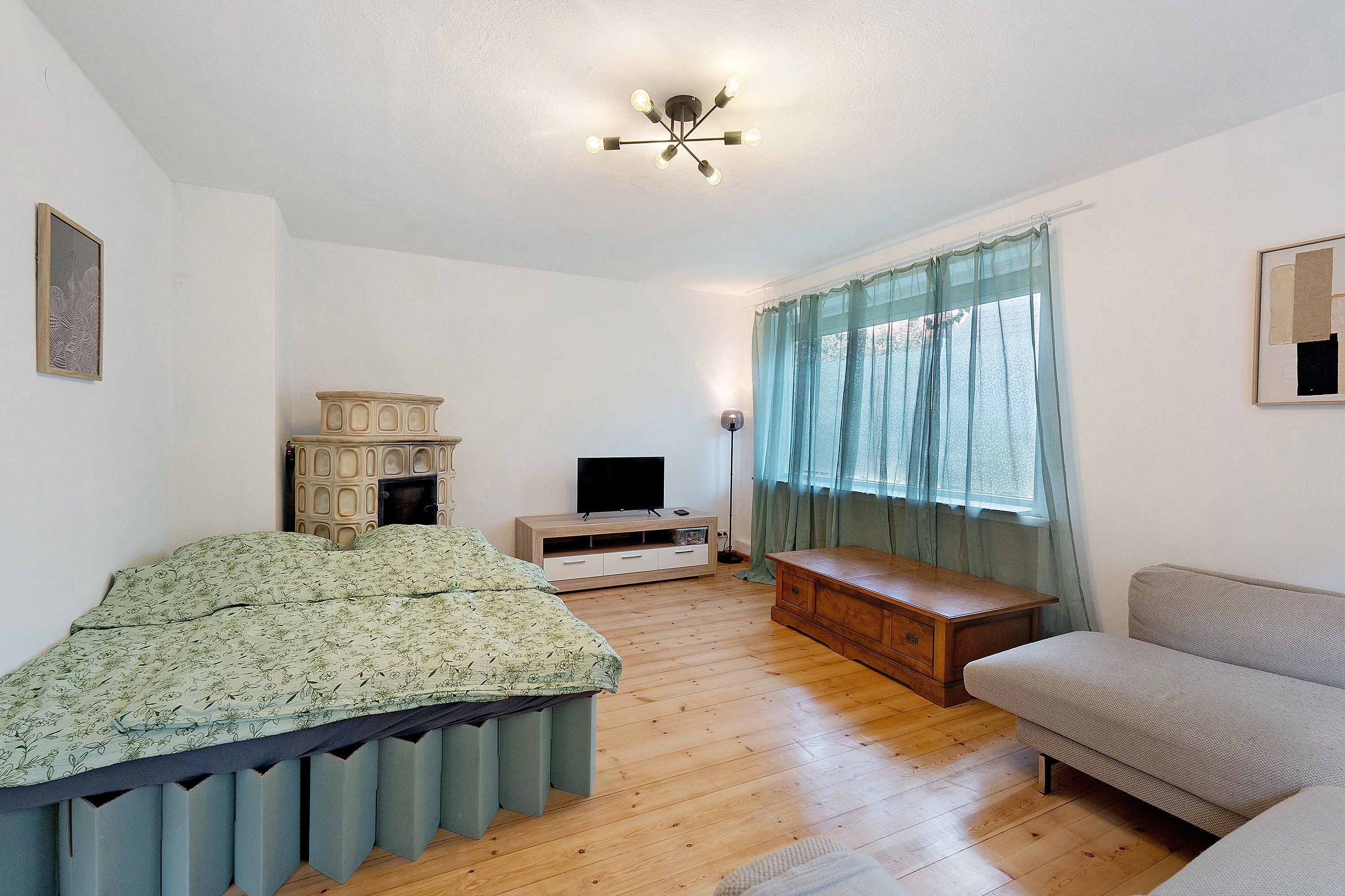 Ein Schlafzimmer mit einem Bett, einem Fernseher, einer Holzkommode, einem Sofa und einem Fenster mit Vorhängen.