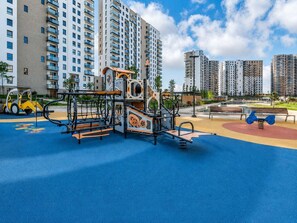 Ein Spielplatz mit Klettergerüsten und Basketballfeld, umgeben von Hochhäusern.