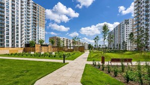 A pathway leading to a residential area with modern apartment buildings, a grassy lawn, and a wooden fence. - Letnica 159 | Sea View | 2 Bedrooms (Gdańsk)