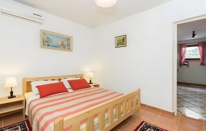 Un dormitorio con una cama de madera, dos lámparas de noche, una mesita de noche, una ventana con cortinas y una puerta que da a otra habitación.