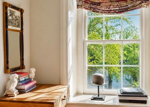 A room with a large window, a wooden desk, a mirror, books, and a decorative owl.