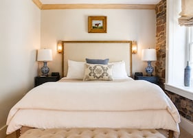 Uma cama com cabeceira de madeira, duas luminárias de apoio e um quadro na parede.