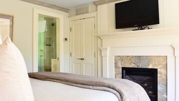 Quarto com cama, televisão sobre lareira e porta para banheiro.