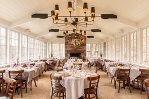 A restaurant with multiple tables, a stone fireplace, and a chandelier.