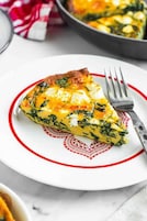 Uma fatia de quiche em um prato branco com borda vermelha.