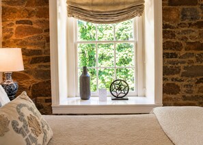 A room with a stone wall, a window with a view of greenery, a vase, and a decorative metal piece.