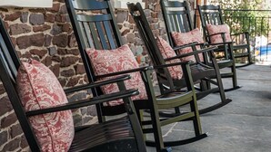 A row of rocking chairs with patterned cushions, positioned outside a stone building with white-framed windows. - Golden Pheasant Inn (Erwinna)