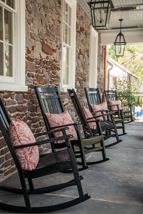 A row of rocking chairs with patterned cushions, positioned outside a stone building with white-framed windows.