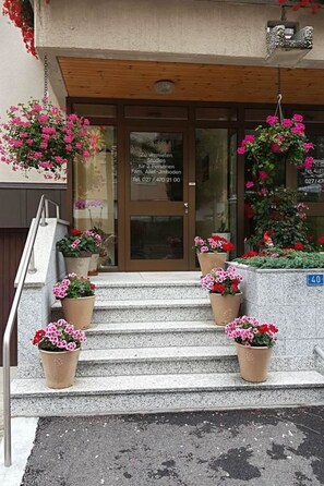 A building entrance with a wooden staircase, potted flowers, and a sign with contact information. - Bergtreu 13 # 2-bed apartment, Dusche, WC 2-Bettwohnung, Dusche, WC by Interhome (Leukerbad)