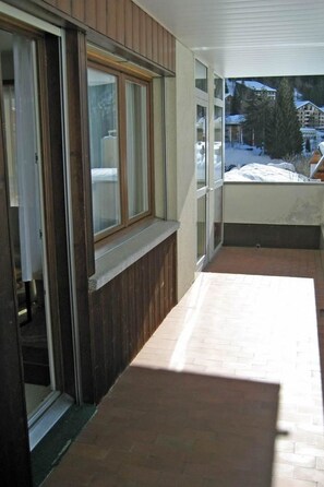 Un balcón con vista a un paisaje nevado, una pared exterior de madera y un ventanal que da a una habitación.