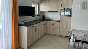 Eine moderne Küche mit hellen Holzschränken, einer schwarzen Arbeitsplatte, einem eingebauten Backofen und einem Fenster mit Vorhängen.