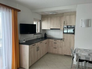 A modern kitchen with light wood cabinets, a black countertop, a built-in oven, and a window with curtains. - Bergtreu 13 # 2-bed apartment, Dusche, WC 2-Bettwohnung, Dusche, WC by Interhome (Leukerbad)