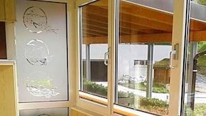 Ein Zimmer mit Holzboden, einem Tisch mit Blumenmuster, zwei Stühlen und einem Fenster mit Blick nach draußen.