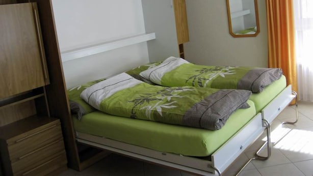Ein Doppelbett mit grüner Bettwäsche und zwei Kissen, ein Holzschrank, ein Spiegel und ein Fenster mit Vorhängen.