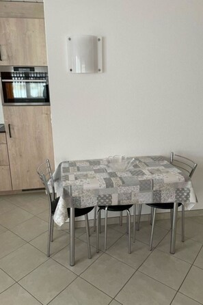 A dining area with a table covered in a patchwork tablecloth, four metal chairs, and a kitchen with a microwave and oven in the background. - Bergtreu 13 # 2-bed apartment, Dusche, WC 2-Bettwohnung, Dusche, WC by Interhome (Leukerbad)