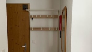 Ein schmaler Gang mit einer Holztür, einer weißen Bank und einem Spiegel an der Wand.