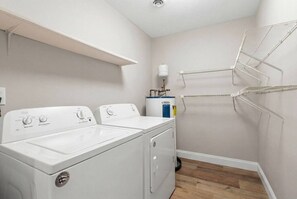 A laundry room with a front-loading washer and dryer, a water heater, and a drying rack. - Infinity Dream𓇼Ocean Views+Sleeps 14+Golf Cart (Oak Island)